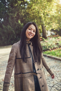 Beautiful middle-aged japanese woman in stylish coat in autumn park, smiling. sunlight, copy space