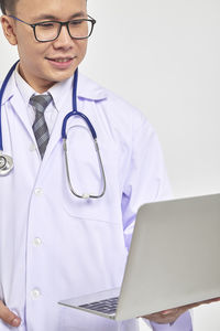 Portrait of smiling doctor holding laptop against white background