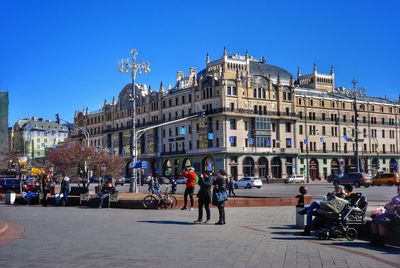 People on street by buildings against clear sky