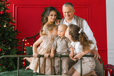 Stylish family with three children is sitting on a bed near a christmas tree. cozy christmas holiday