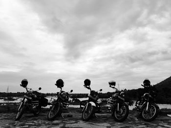 Motorcycles parked by lake against cloudy sky