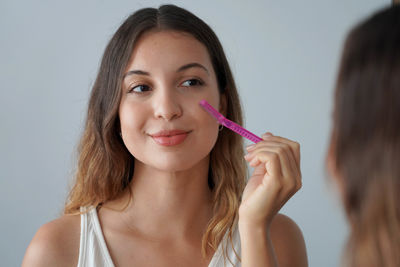 Portrait of young woman applying make-up against wall