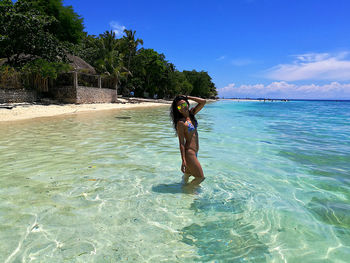 Full length of woman in bikini on sea shore against sky