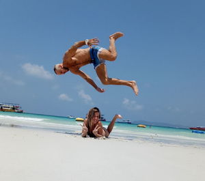 Full length of man jumping over woman at beach during sunny day