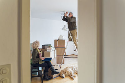 Senior couple in a new home with man mounting ceiling lamp