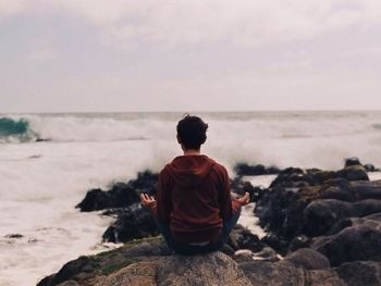 Rear view of woman meditating on rocks at beach