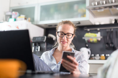 Businesswoman using smart phone sitting at home