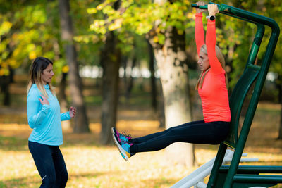 Female friends exercising on outdoor fitness equipment in public park. autumn, fall.