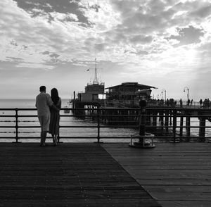 Rear view of couple standing on bridge over sea against sky