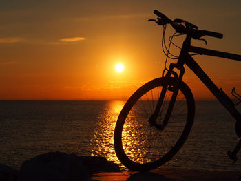 Silhouette bicycle by sea against sky during sunset