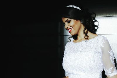 Smiling bride looking down while standing against wooden wall