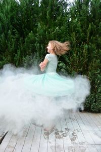 Side view of happy girl spinning with smoke against plants at park