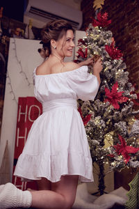 Portrait of smiling young woman standing against christmas tree