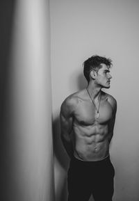 Young man looking away while standing against wall