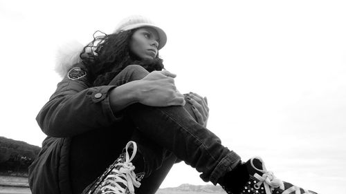 Low angle view of thoughtful woman sitting against clear sky