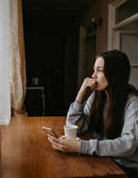 Side view of young woman drinking water at home