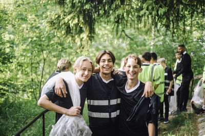 Portrait of smiling male teenage volunteers standing with arms around