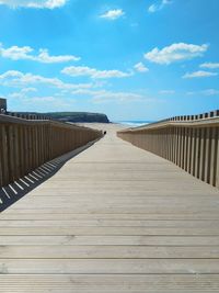 Wooden footbridge on boardwalk against sky