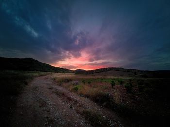 Dirt road on field against sky during sunset