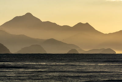 Scenic view of sea and silhouette mountains against clear sky