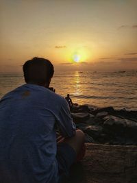 Rear view of man looking at sea against sky during sunset