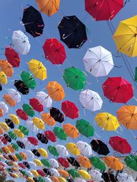 Low angle view of multi colored umbrellas hanging against blue sky