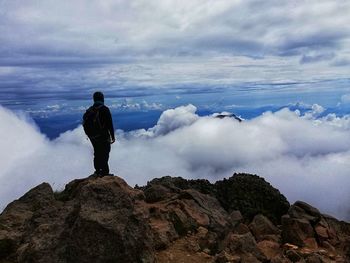 Man standing on rocks against cloudy sky