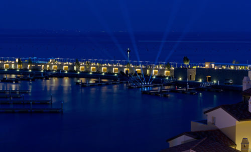 Illuminated buildings by river against sky at night