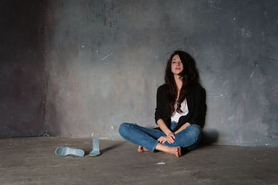 Thoughtful young woman sitting on floor by wall