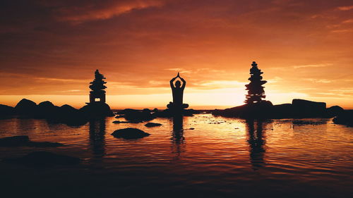 Silhouette man practicing yoga while sitting on rock by lakeshore