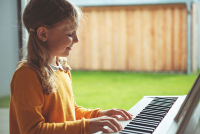 Side view of girl playing piano while siting at home