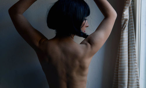 Rear view of shirtless woman standing at home