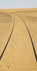 Tire tracks on desert land against clear sky