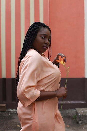 Portrait of young woman standing on road against wall