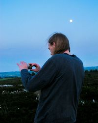 Rear view of man photographing from mobile phone against sky at twilight