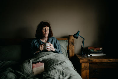 Woman holding coffee cup resting on bed at home