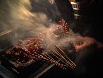 Cropped hand grilling chicken satay on barbecue grill