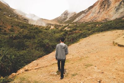 Rear view of man walking on mountain against sky