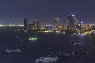 Illuminated city by sea against sky at night