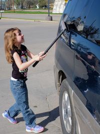 Full length of girl cleaning car window on road