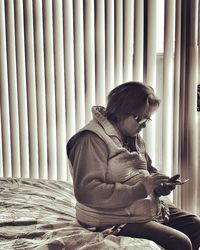 Woman using mobile phone while sitting on bed at home