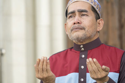 Close-up of mature man praying while sitting at mosque