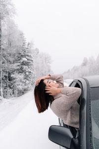 Side view of woman in car against sky during winter