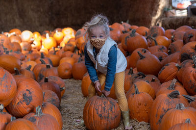 Portrait of smiling girl wearing mask holding pumpkin in farm