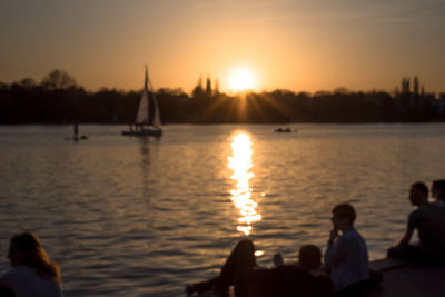 Defocused image of people by lake against sky during sunset