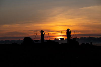 Silhouette people standing on land against sky during sunset