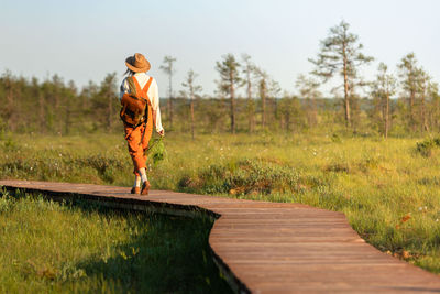 Woman botanist with backpack on ecological hiking trail in summer outdoors. 