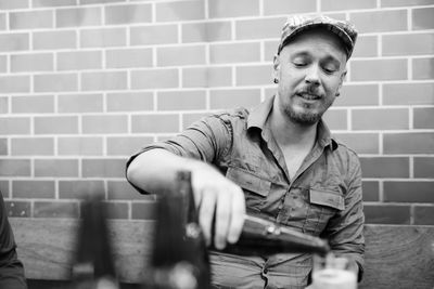 Man pouring alcohol while sitting against wall