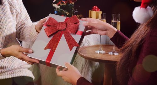 Cropped image of woman giving gift box to friend during christmas