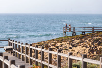 Men standing on railing by sea against sky